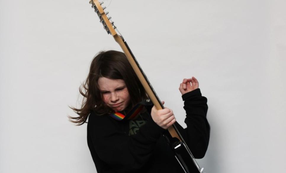 Child with electric guitar strapped playing vigourously